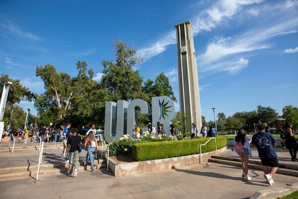 Students walking past UCR sign and bell tower