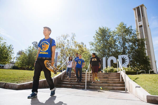 UC Riverside Students Walking By UCR Sign and Bell Tower