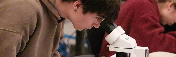 Student in the Genetics and Molecular Biotechnology lab looking through a microscope.